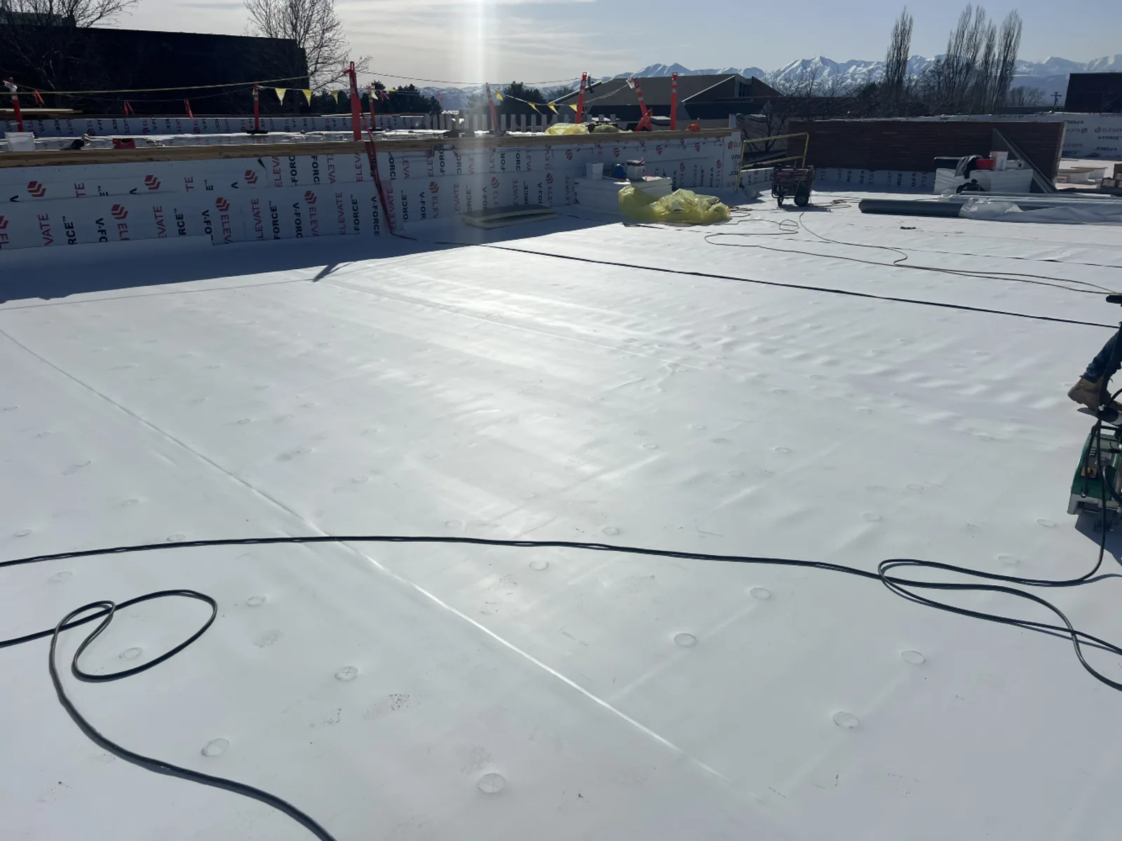 Signature Roofing crew installing a white TPO single-ply membrane roof on a Utah commercial building with mountain backdrop