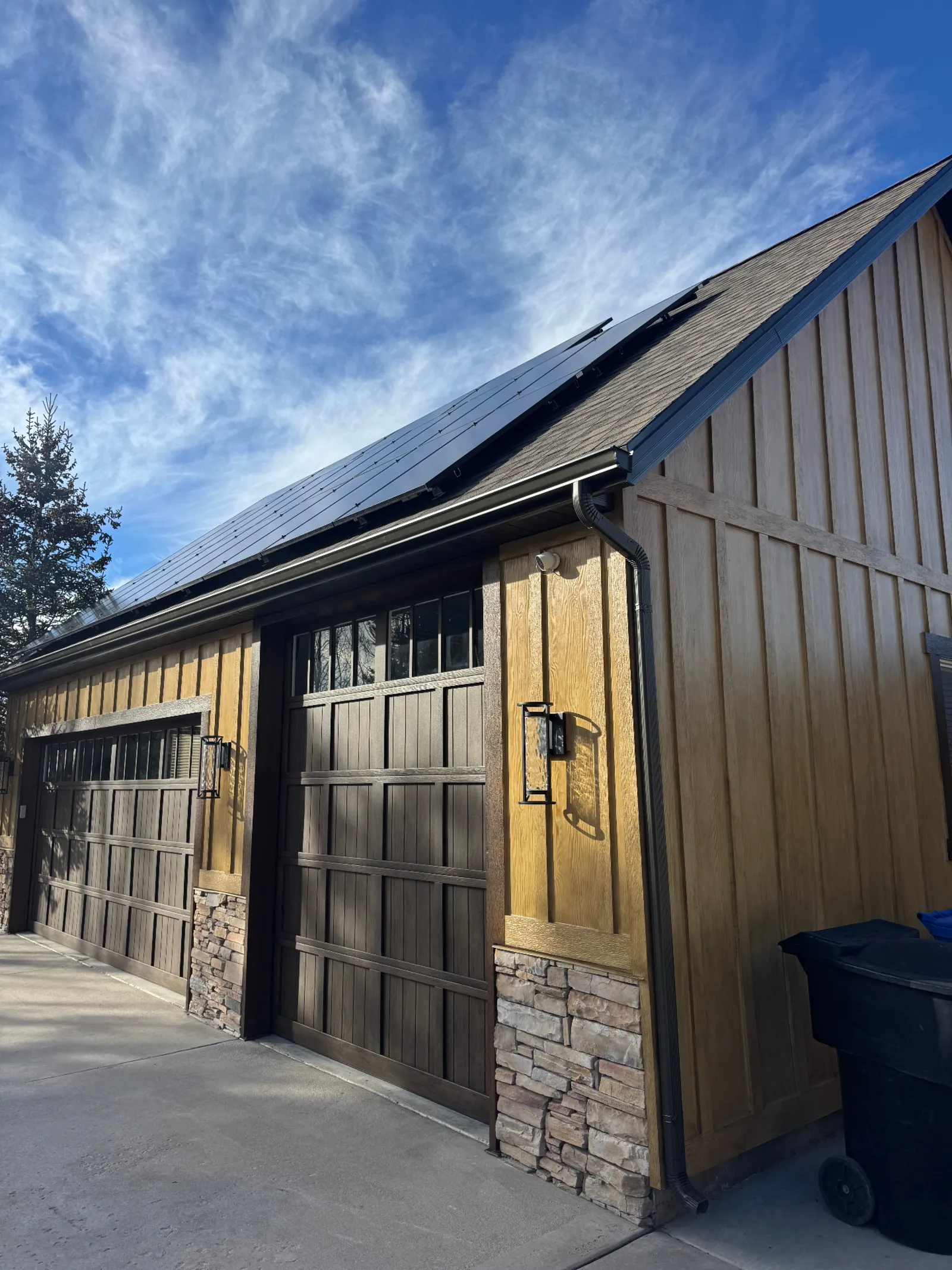 Garage with wood-tone board-and-batten siding, stacked stone wainscot, and rooftop solar panels
