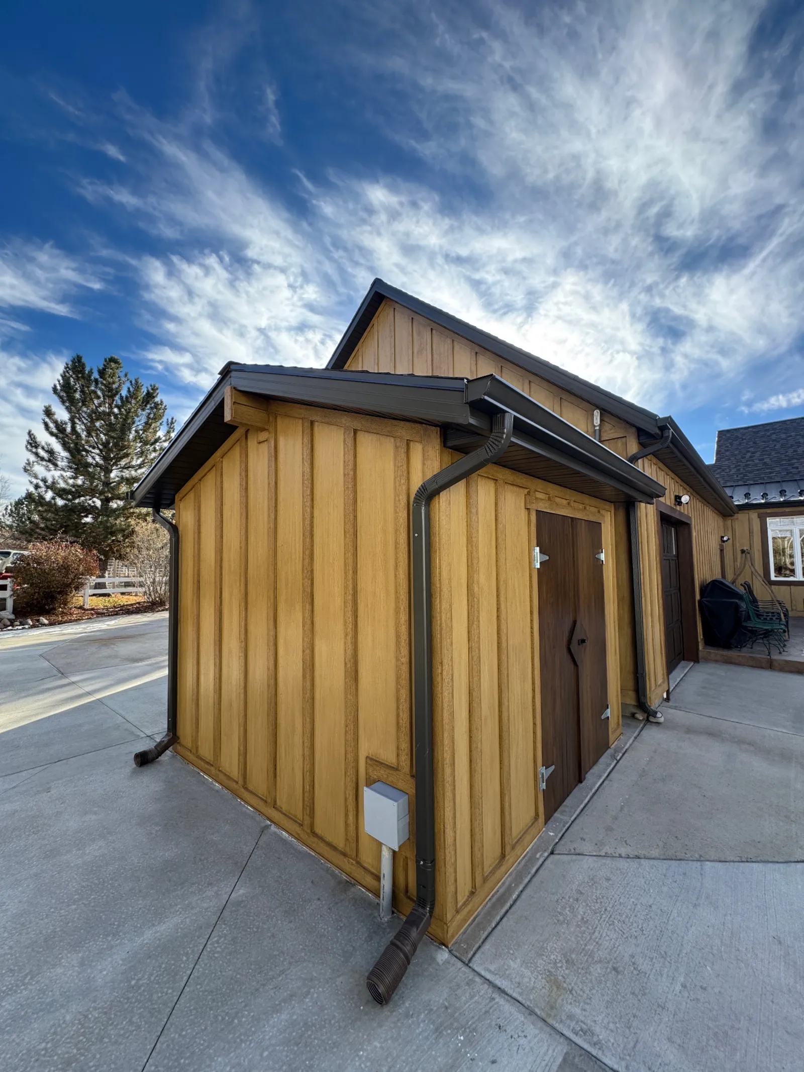 Outbuilding with warm wood-tone board-and-batten siding and dark metal gutters